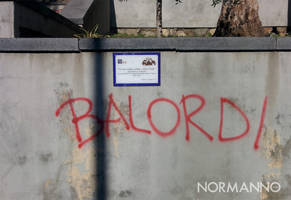 scritta che imbratta il muro su cui è apposta la targa in memoria di Falcone e Borsellino