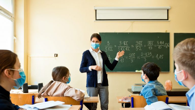foto di una classe con dei bambini e un'insegnante a scuola che indossano le mascherine contro il coronavirus